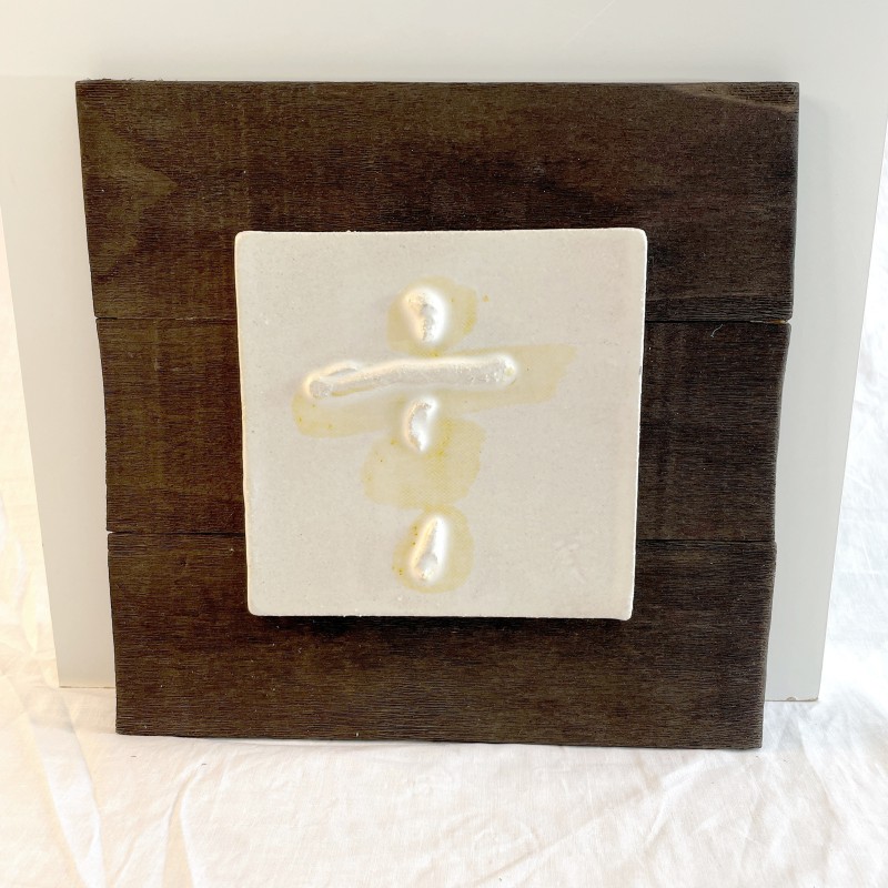 Ceramic relief featuring a vertical abstract figure suggesting a being on a dark wood panel by Ismael Garcia Burillo